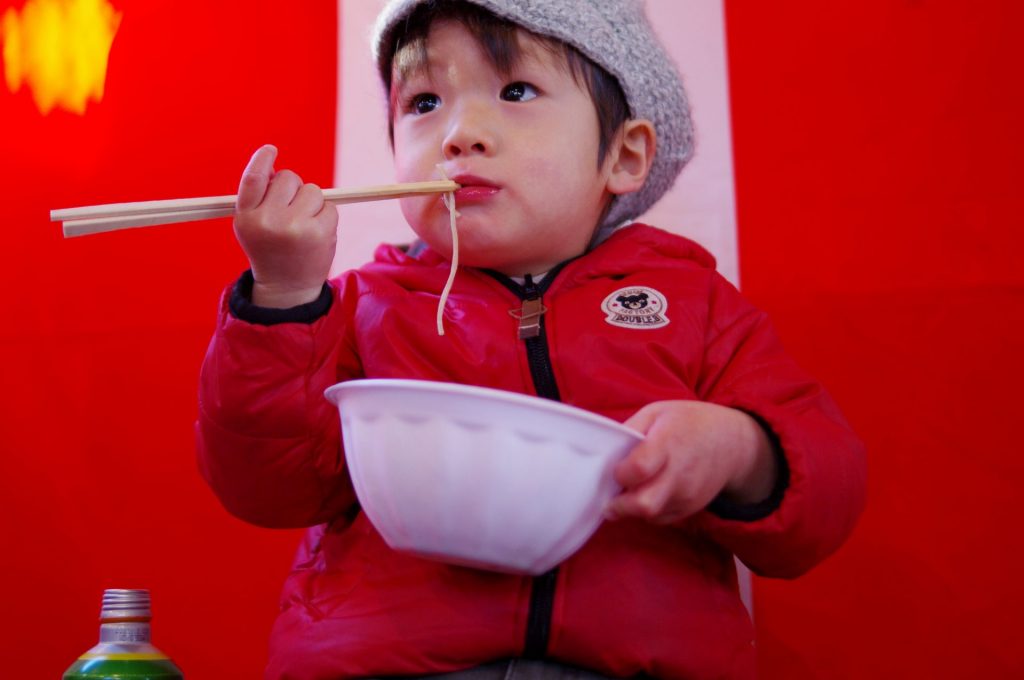 箸とお椀をもって蕎麦を食べている男の子