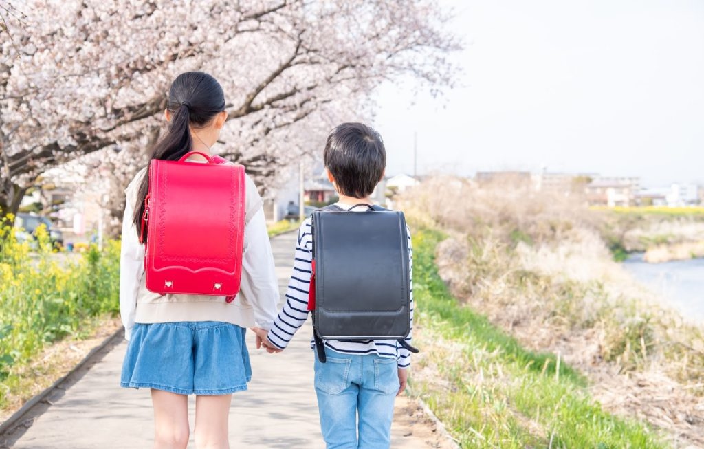 桜の咲く河川敷を手を繋いで歩いている兄弟